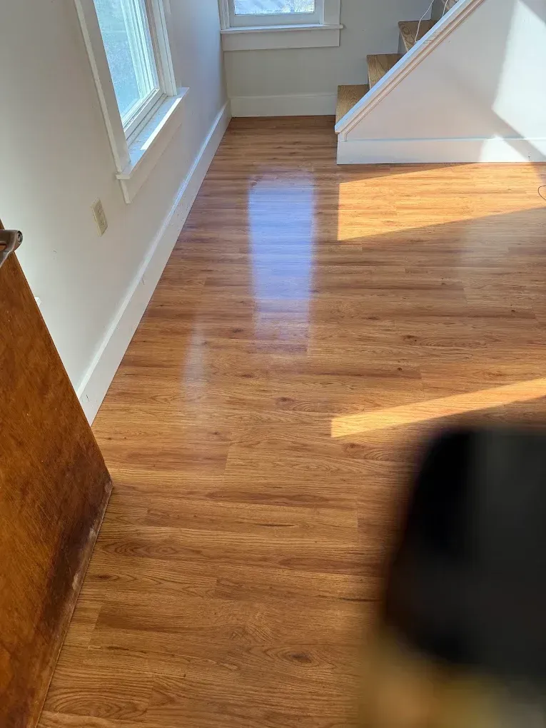 Sunlit hardwood floor in a stair landing with white walls and a window.