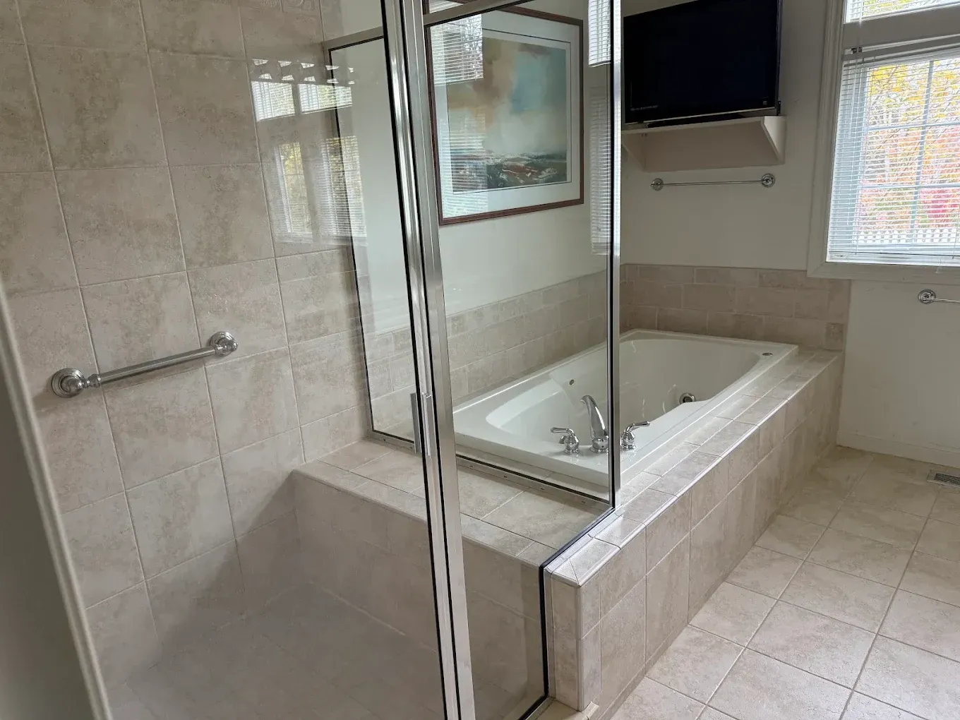 Bathroom with a glass-enclosed jetted tub, tiled walls, and a wall-mounted TV.