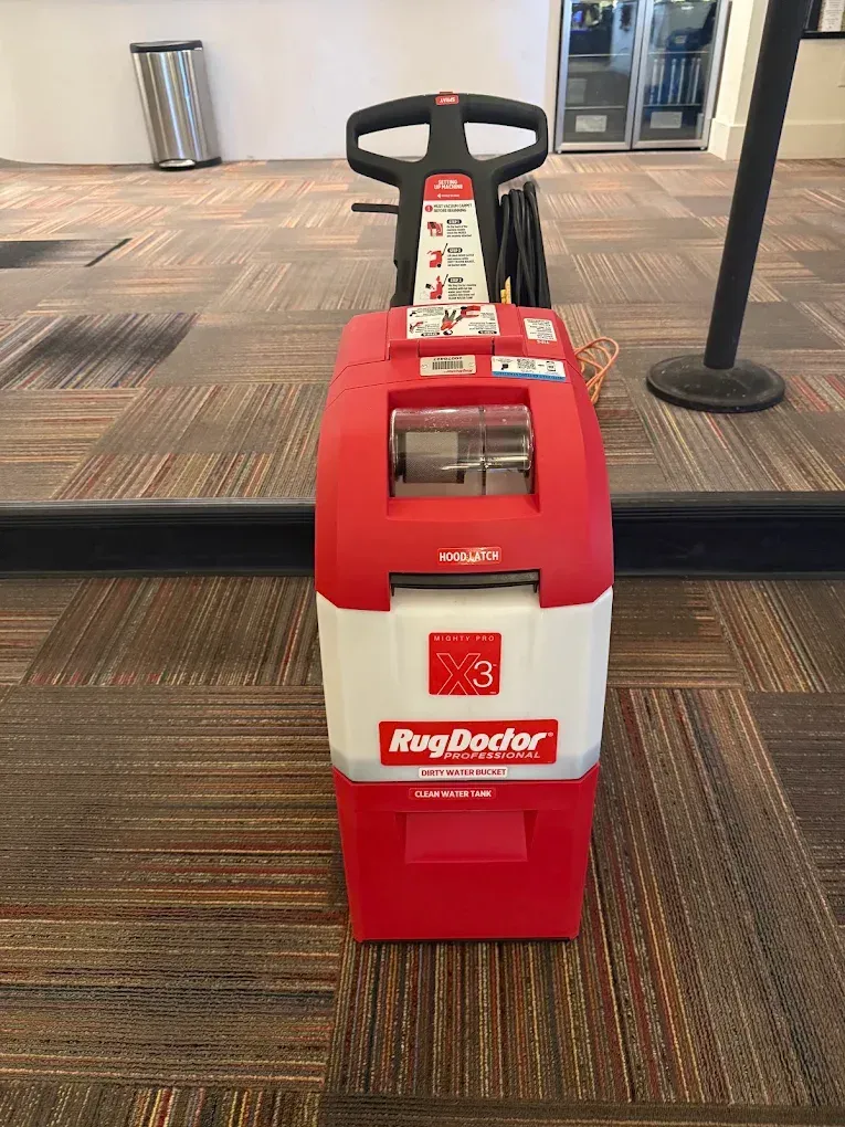 Red Rug Doctor carpet cleaner standing on a carpeted floor in a lobby.