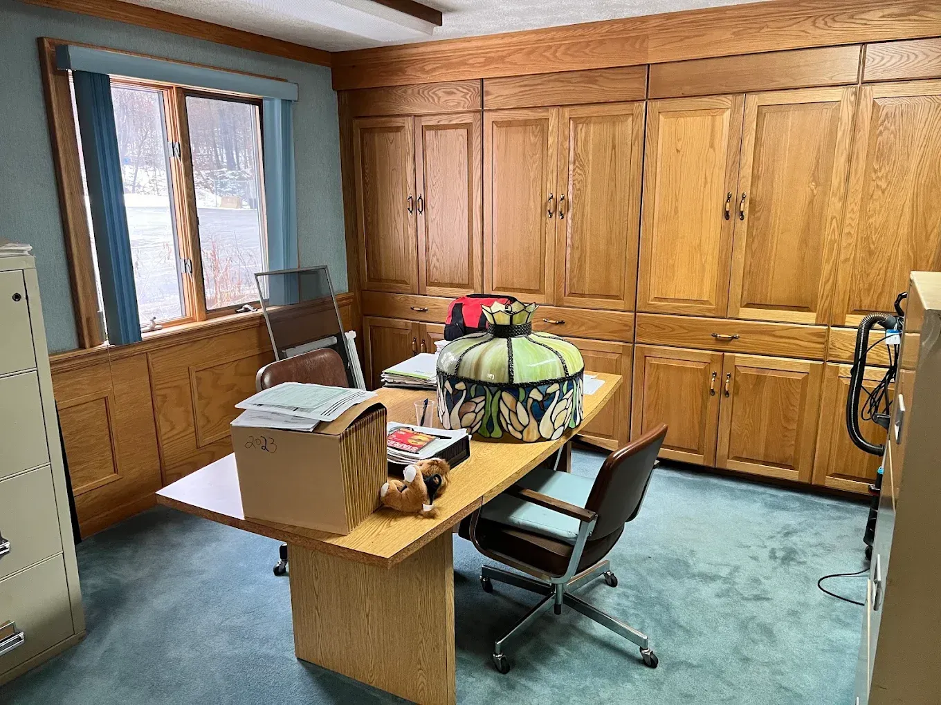 Wood-paneled office with desk, chair, printer, and large cabinets along the wall