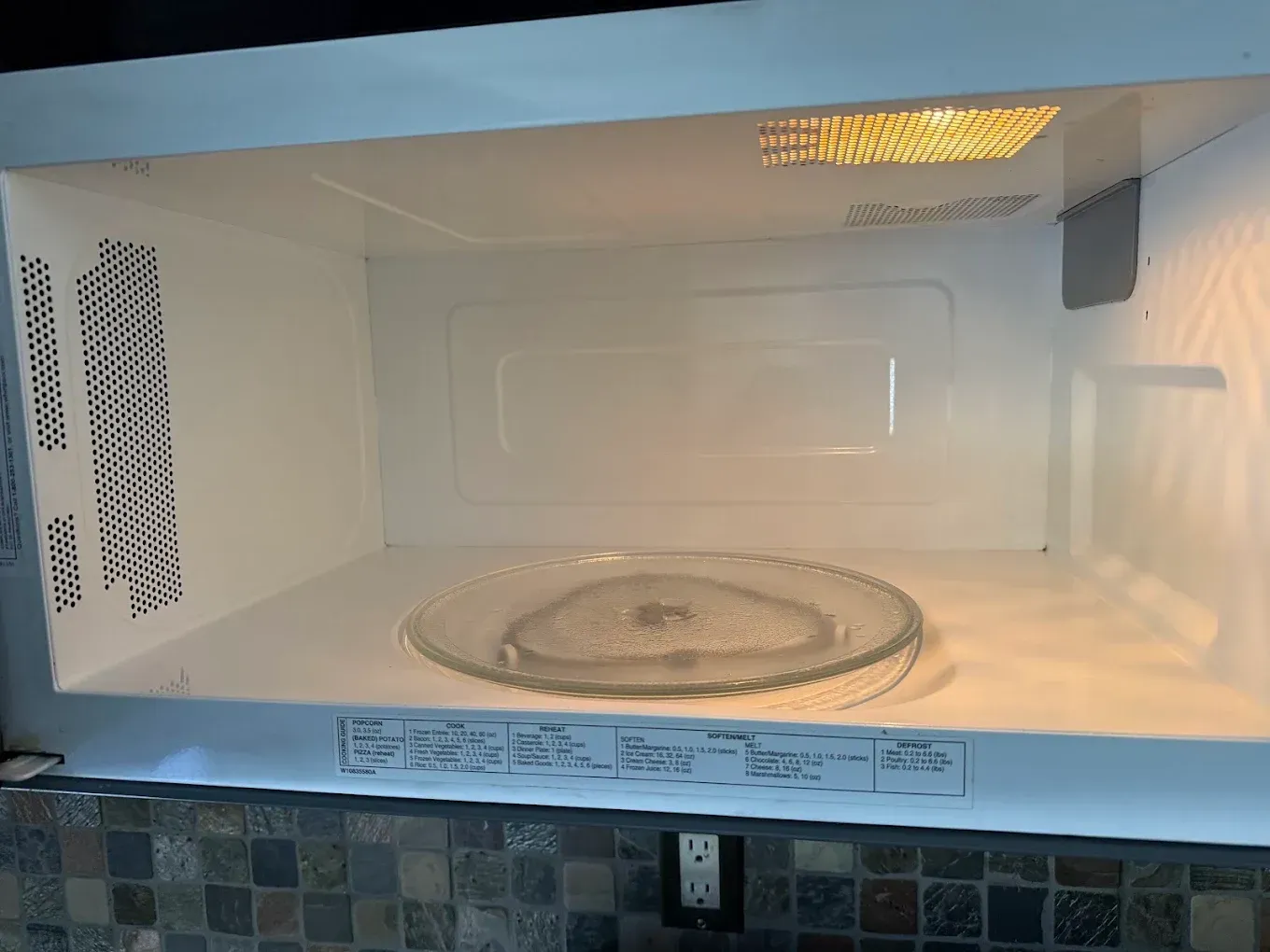 Empty white microwave interior with a glass turntable and a light on the right side.