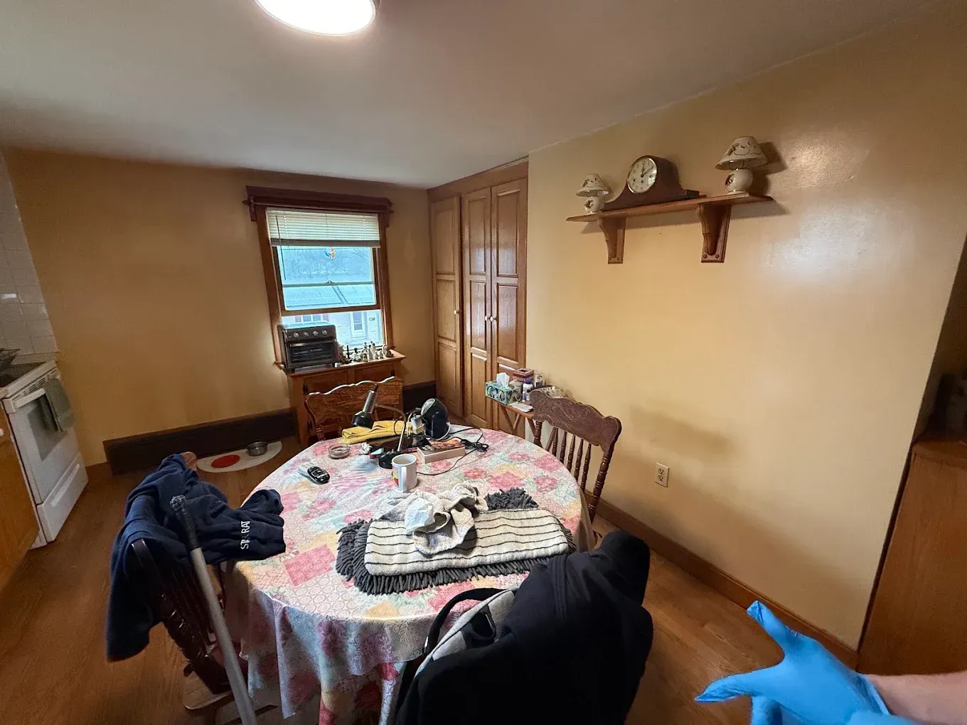 Dining room with round table, chairs, and a window, in a warm tan room with a wall shelf.