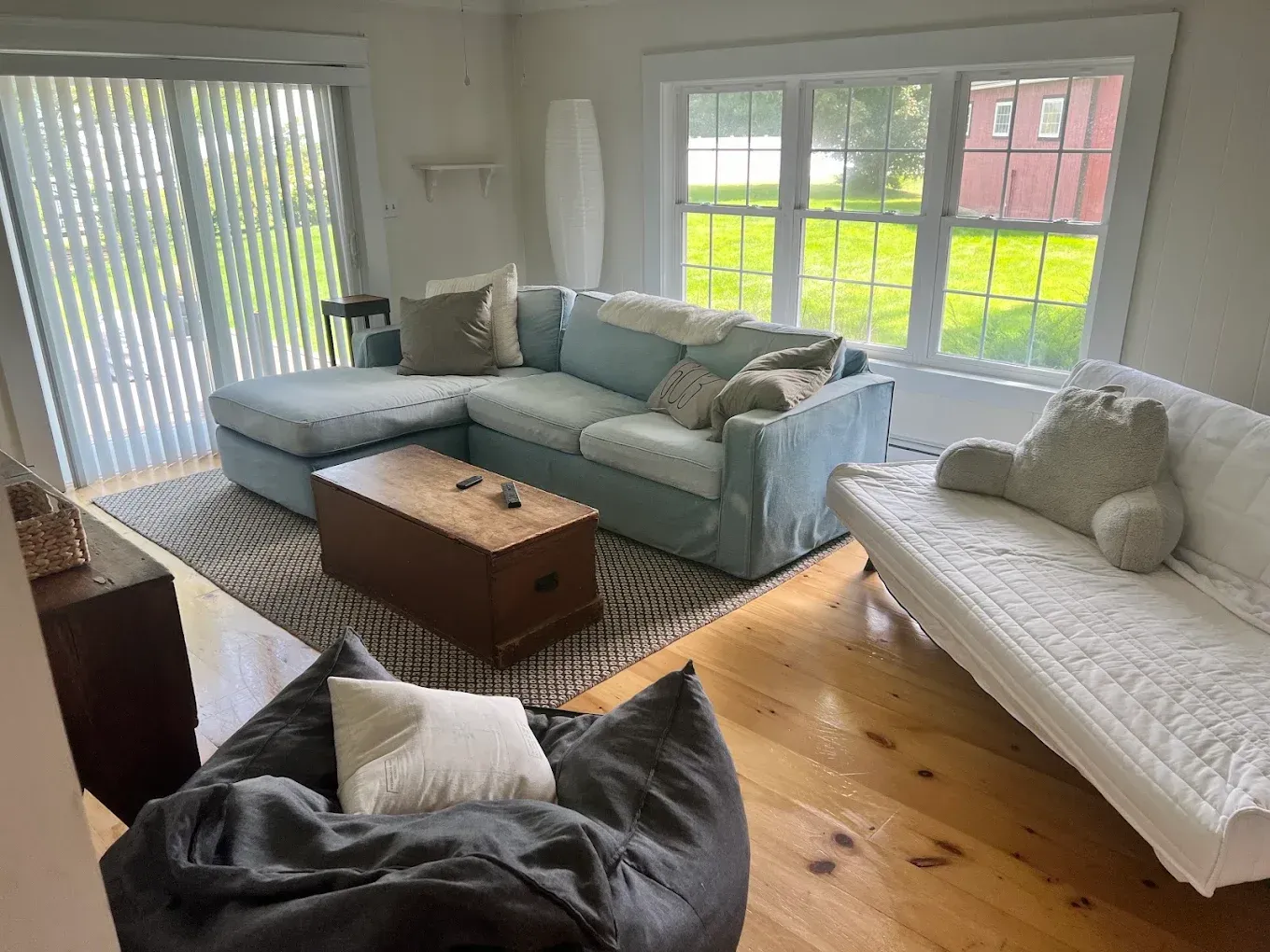 Bright living room with blue and white sofas, a beanbag, coffee table, and large windows with blinds