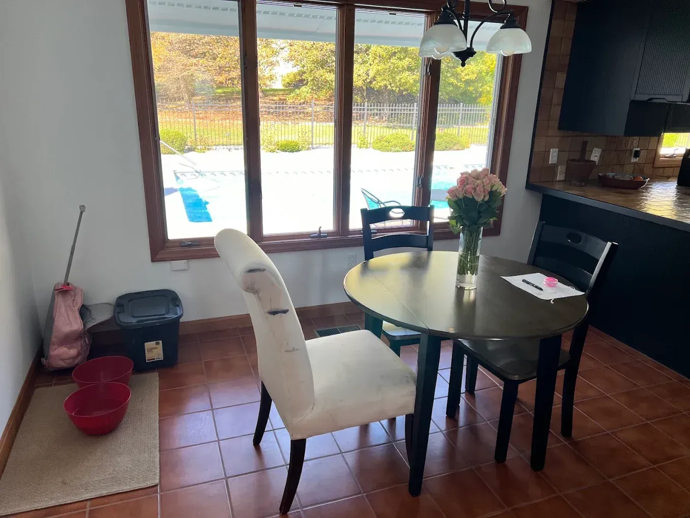 Dining area with round table, white chairs, and large window overlooking a patio and pool
