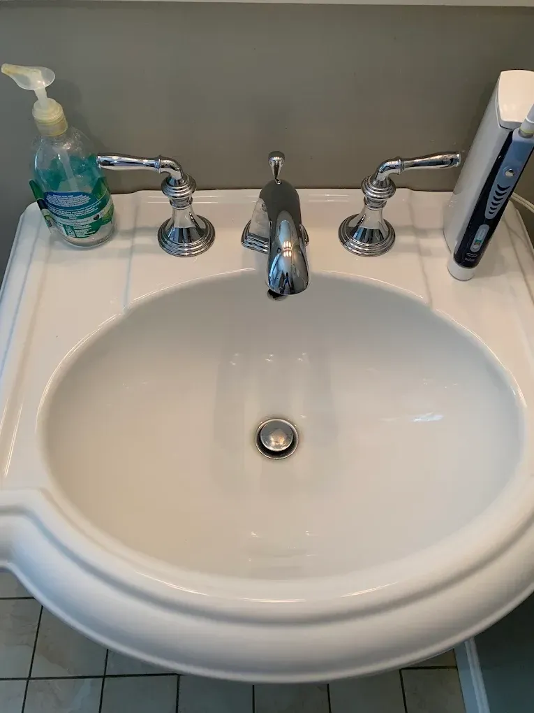 White bathroom sink with chrome faucet, soap dispenser, and toothbrush holder on the counter.
