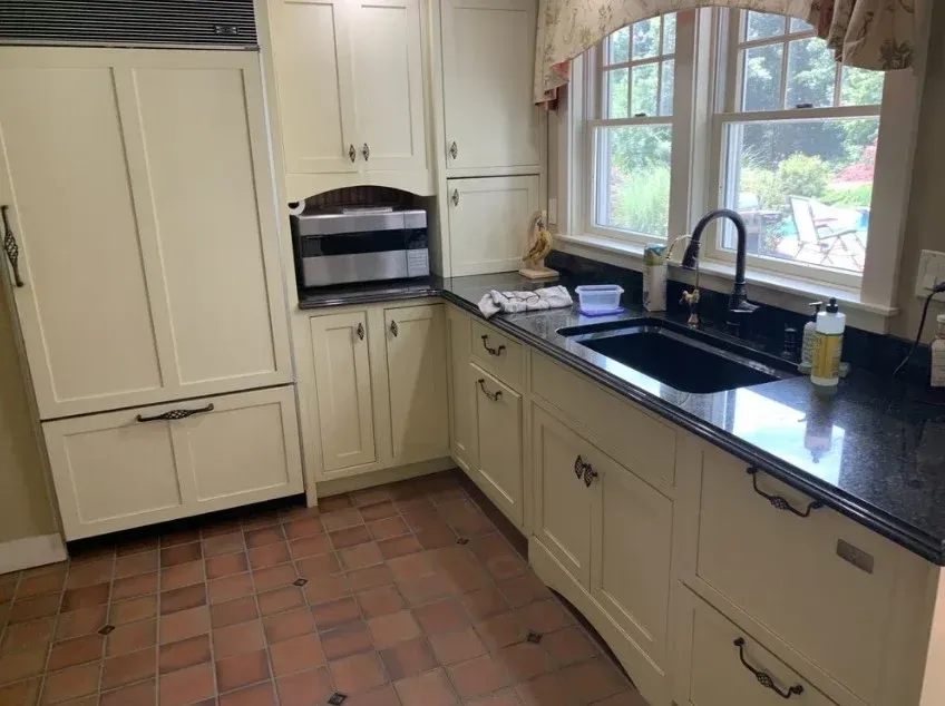 Bright kitchen with cream cabinets, black countertops, tiled floor, and a window over the sink.