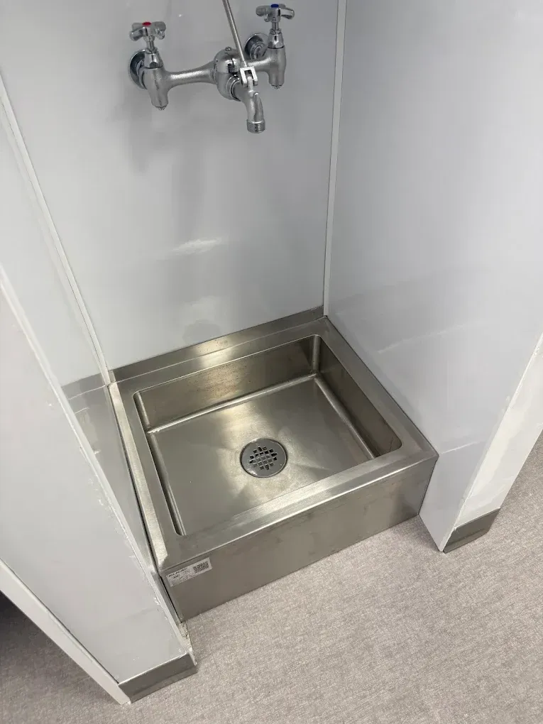 Stainless steel accessible shower pan with wall-mounted faucet in a small tiled corner alcove