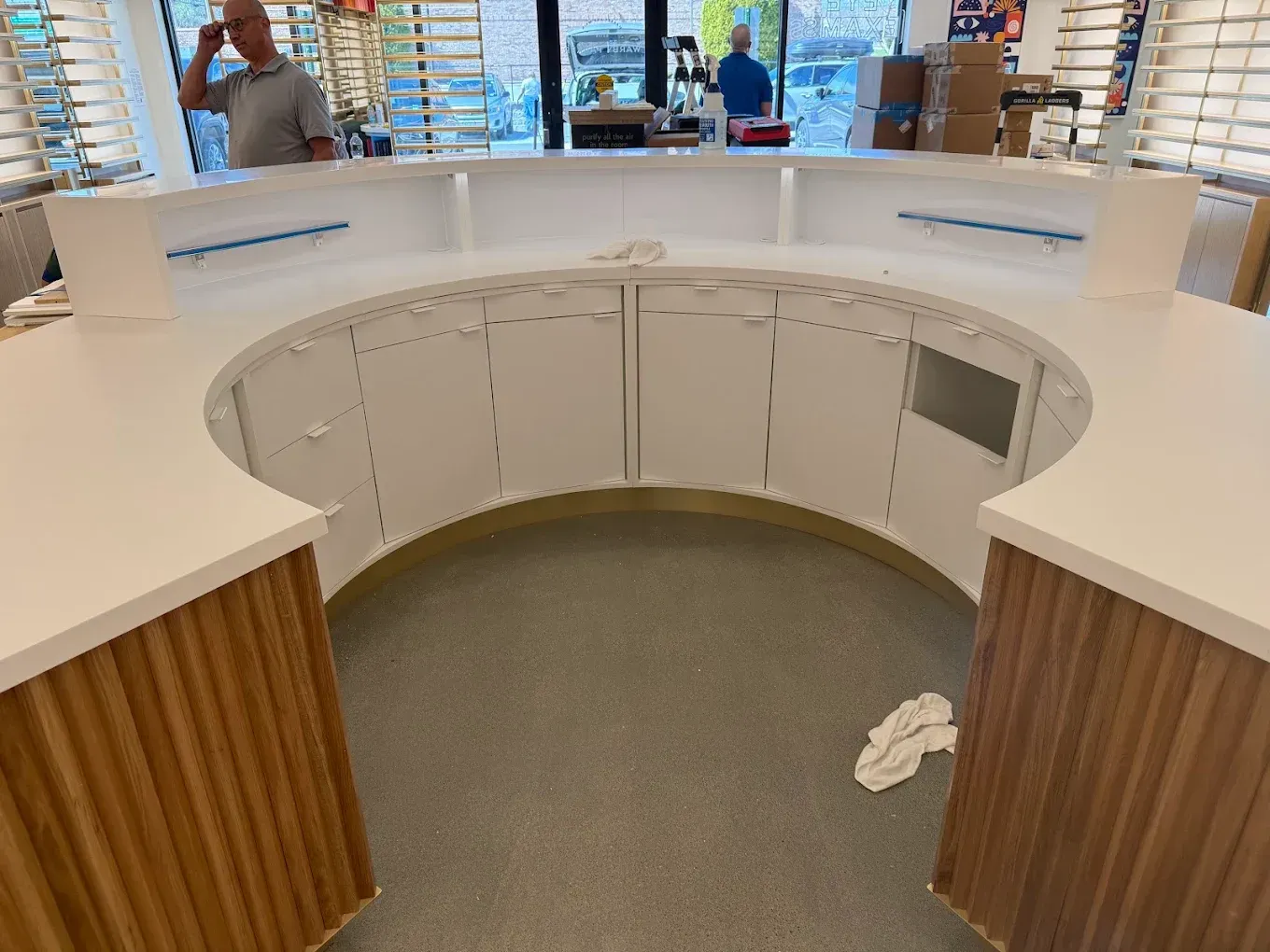Curved white retail counter with wood paneling and open storage, viewed from above in a store interior.
