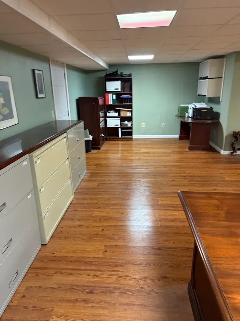 Empty office hallway with wood floors, filing cabinets, and desks under ceiling lights