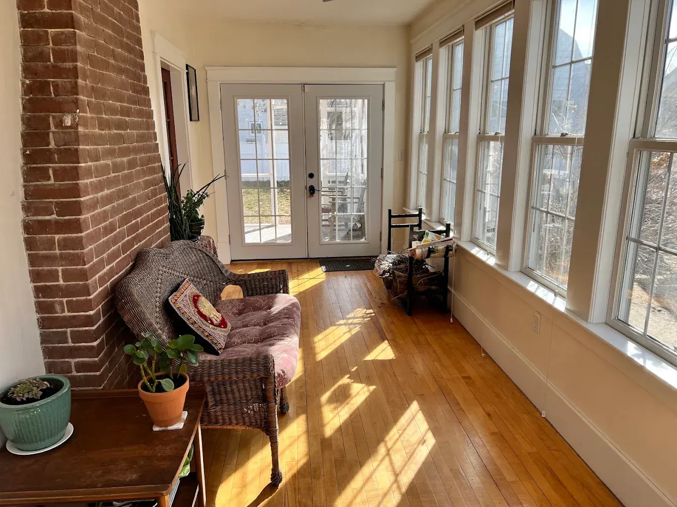 Sunlit enclosed porch with wicker chair, potted plants, and French doors overlooking outdoors