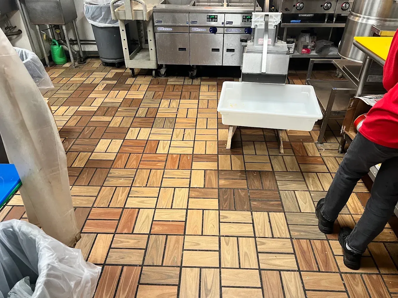 Commercial kitchen with checkered tile floor, stainless steel counters, and a person standing at right.