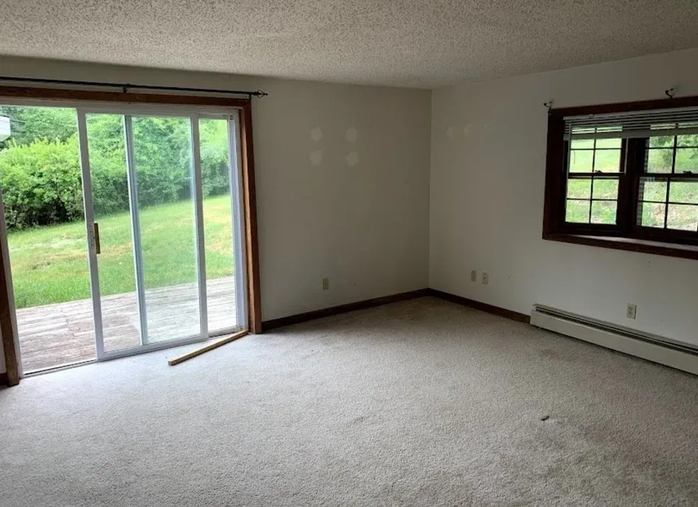 Empty carpeted living room with sliding glass doors and a view of the green yard