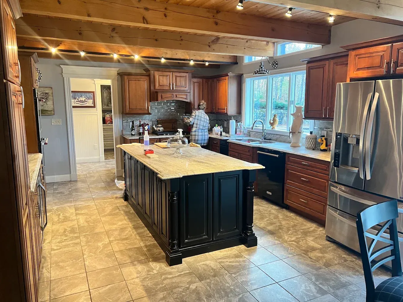 Modern kitchen with dark wood cabinets, large island, stainless fridge, and a person at the sink