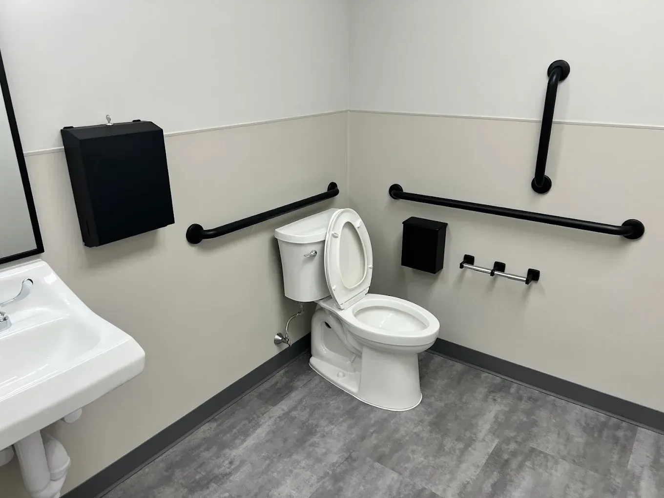 Accessible bathroom with toilet, sink, and black grab bars along the walls
