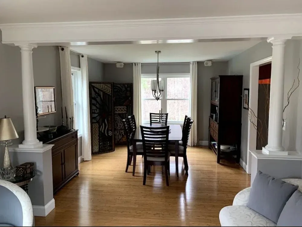 Dining room with dark wood table and chairs, light blue walls, hardwood floors, and a large window at the back.