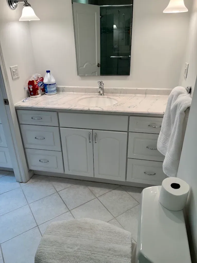 Bathroom vanity with double sink, mirror, wall lights, white cabinet, and tiled floor.