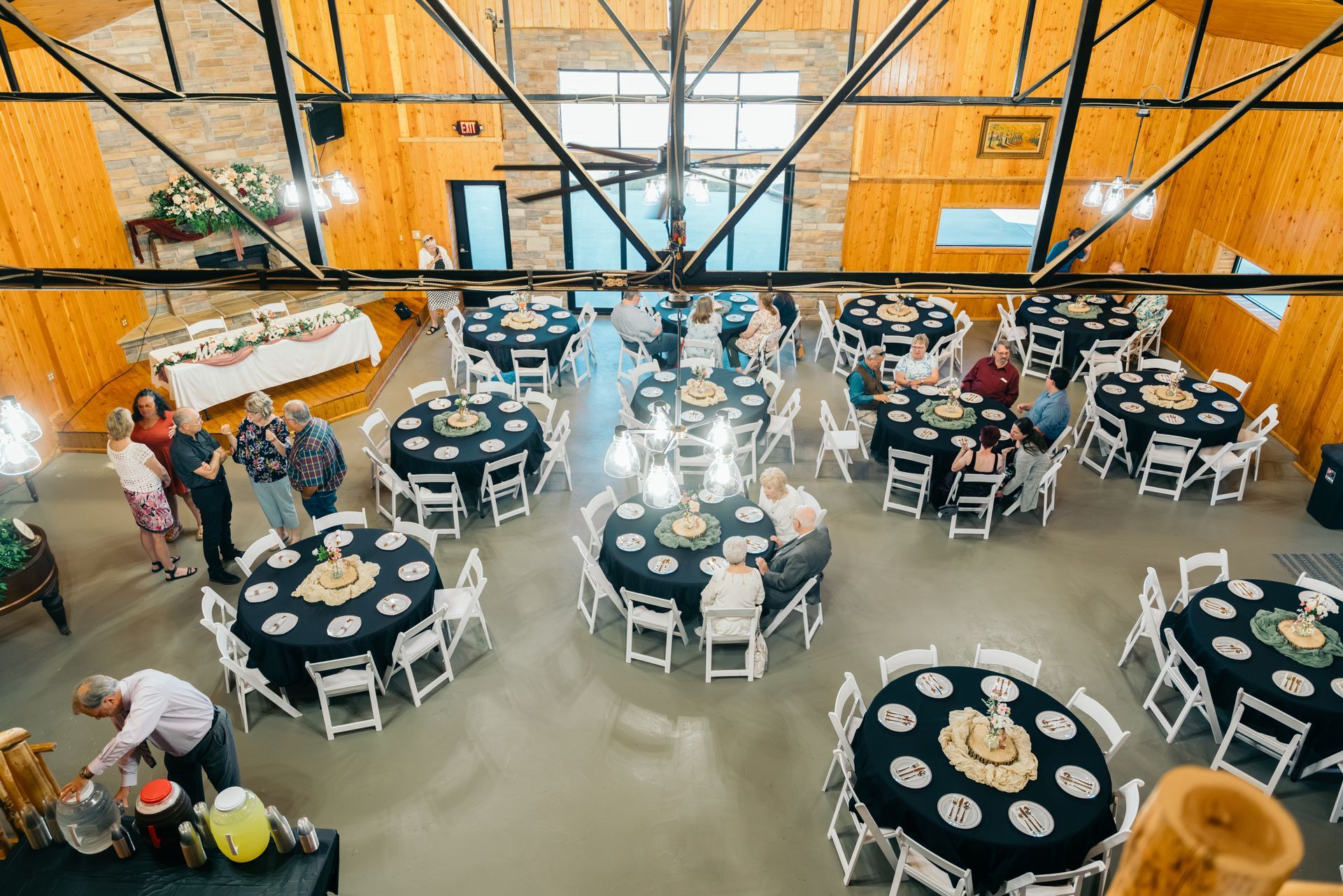 Banquet hall with round tables, white chairs, and guests dining under high industrial ceilings