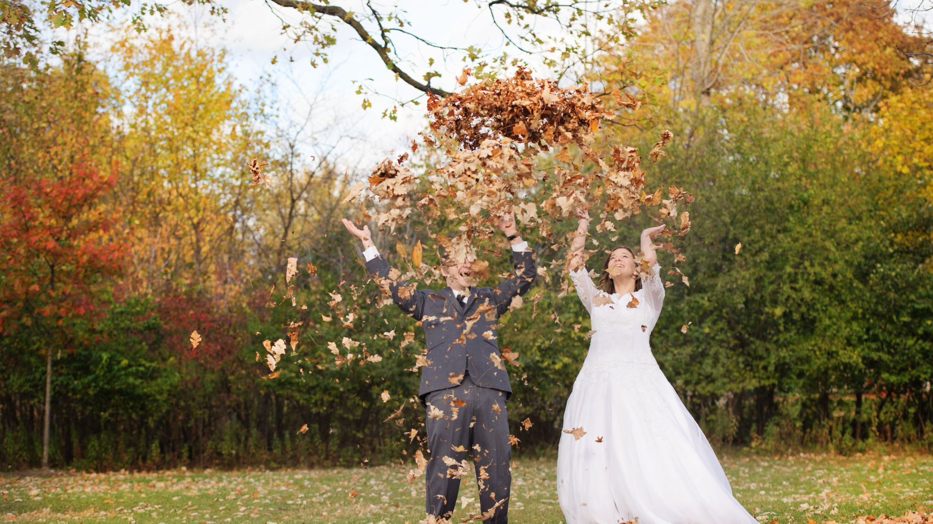 Newlyweds tossing autumn leaves in a colorful garden, bride in white gown and groom in a dark suit