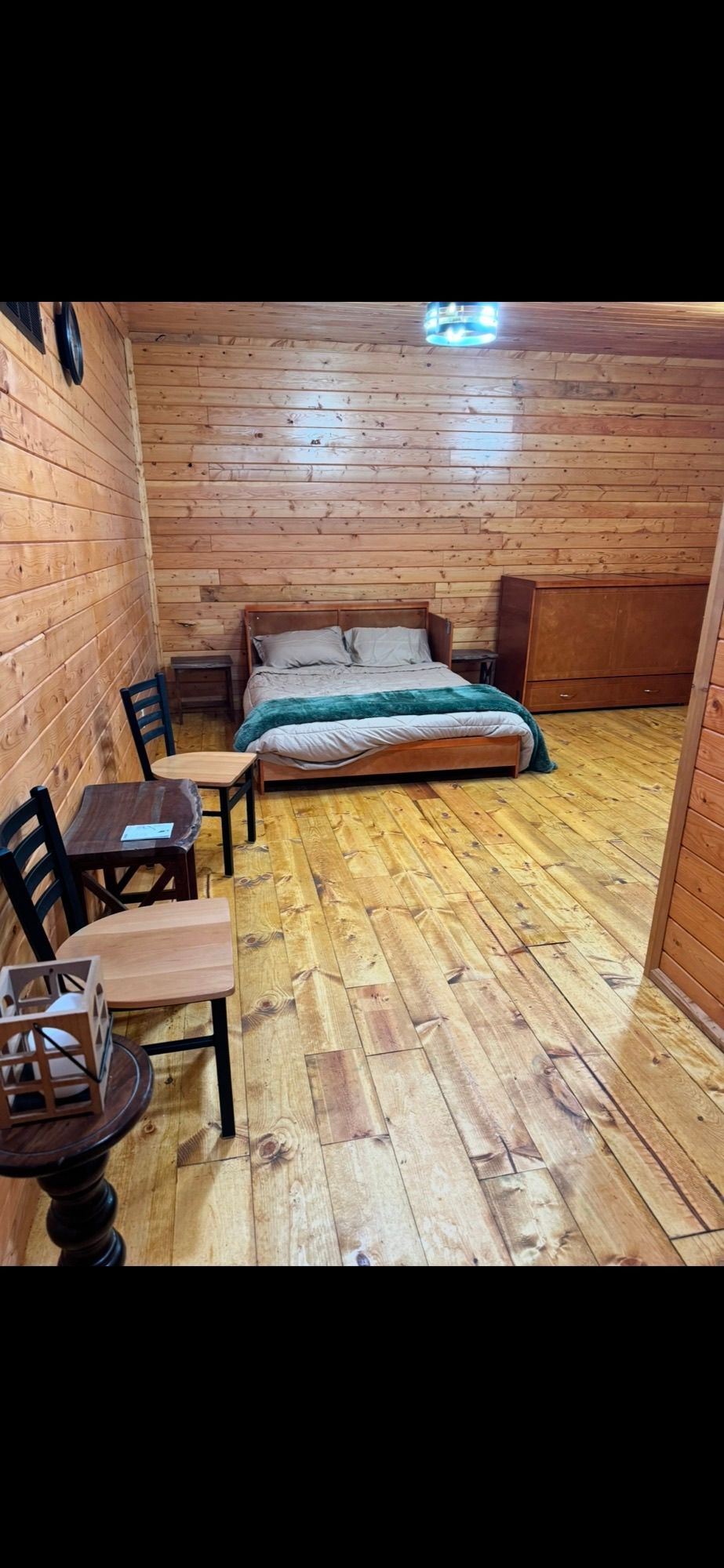Bedroom with wood-paneled walls and floor, bed, chairs, and small table. Bedroom with wood-paneled walls and floor, bed, chairs, and small table.