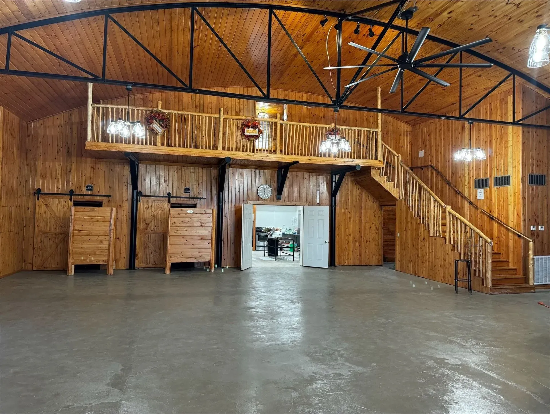 Empty wooden hall with high ceiling, loft railing, staircase, and large open floor.