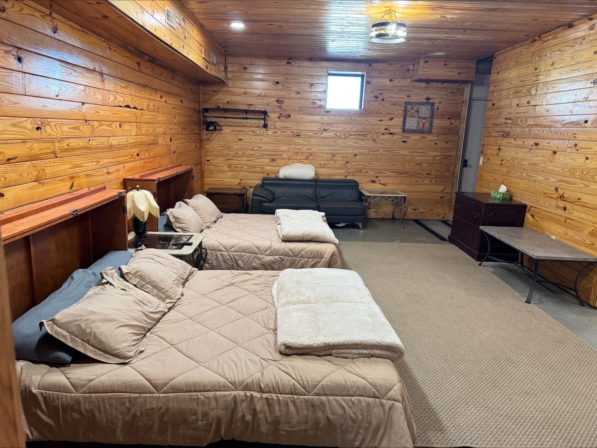 Bedroom with wood-paneled walls, two beds, a couch, and a small window.