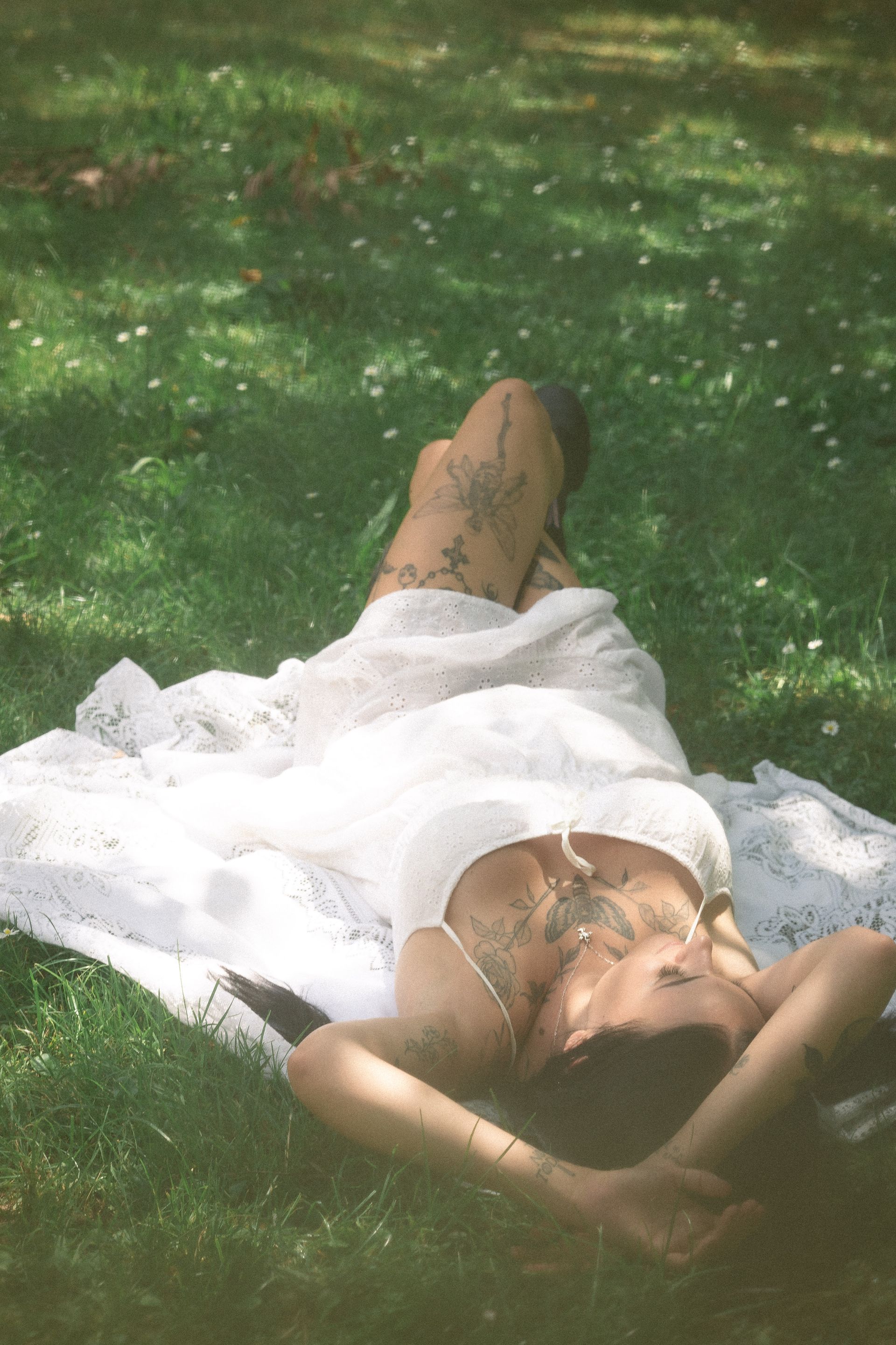 A woman in a white dress is laying on a blanket in the grass.
