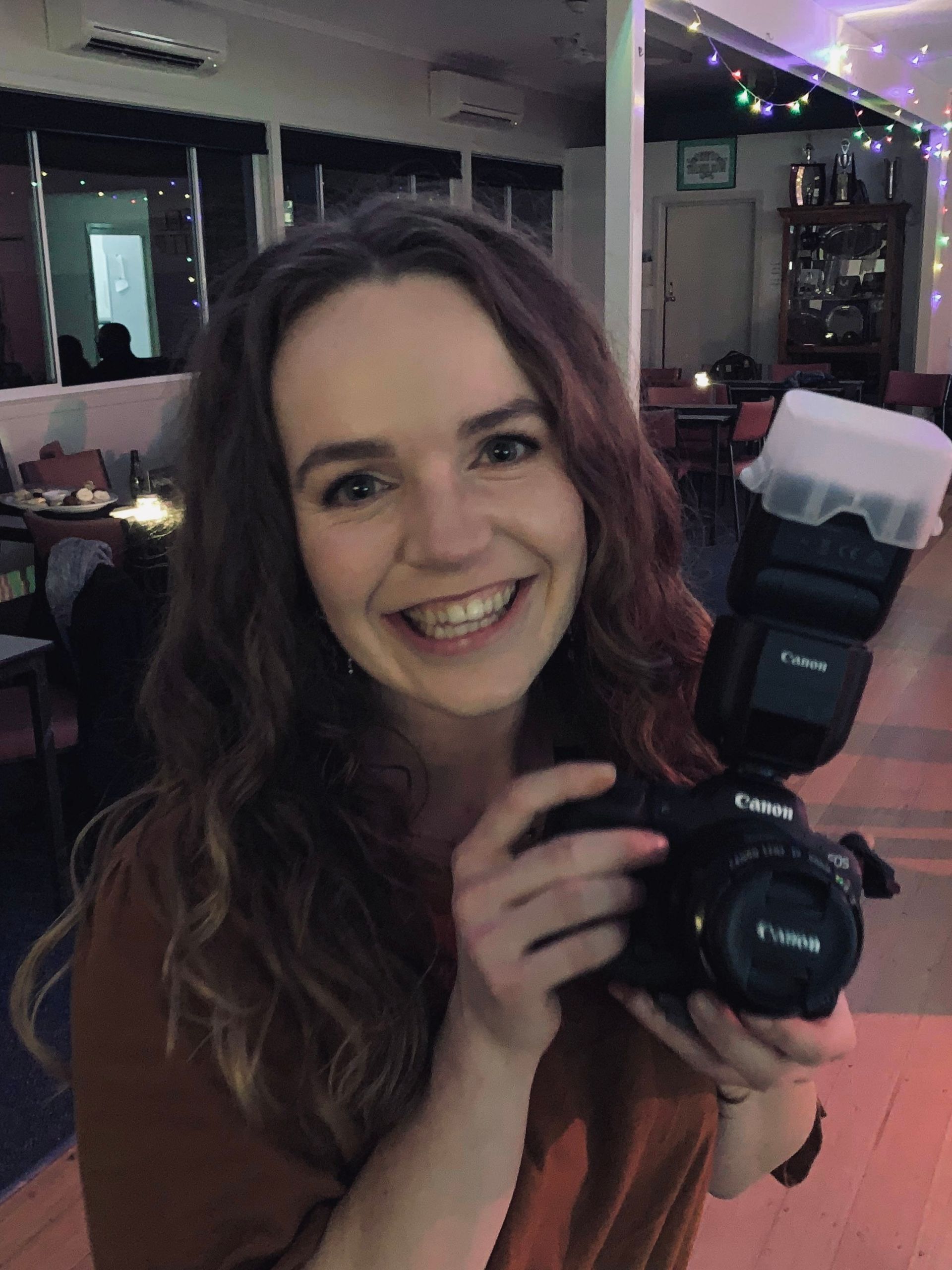 A woman is smiling while holding a canon camera