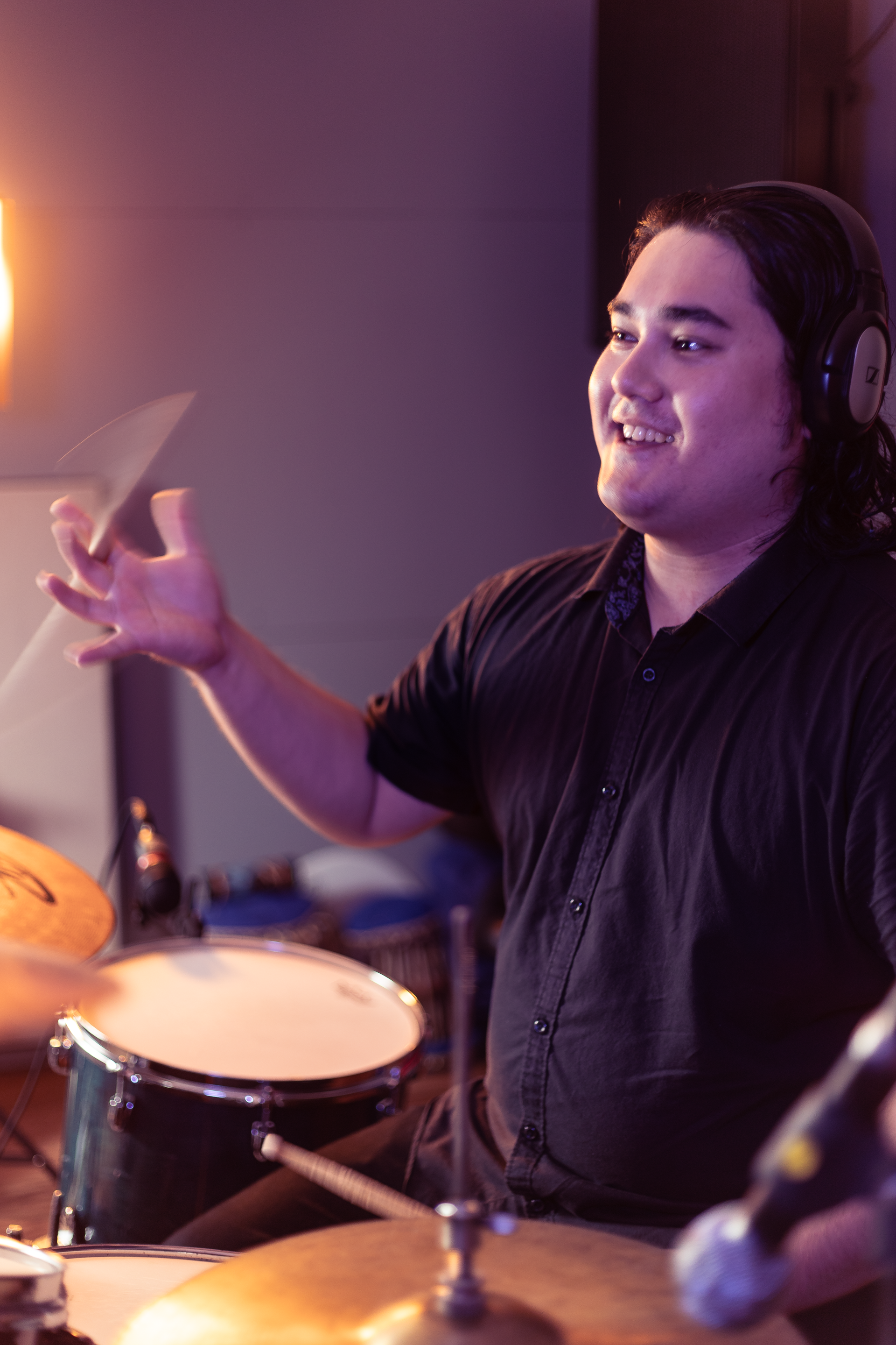 A man in a black shirt is playing drums in a dark room.