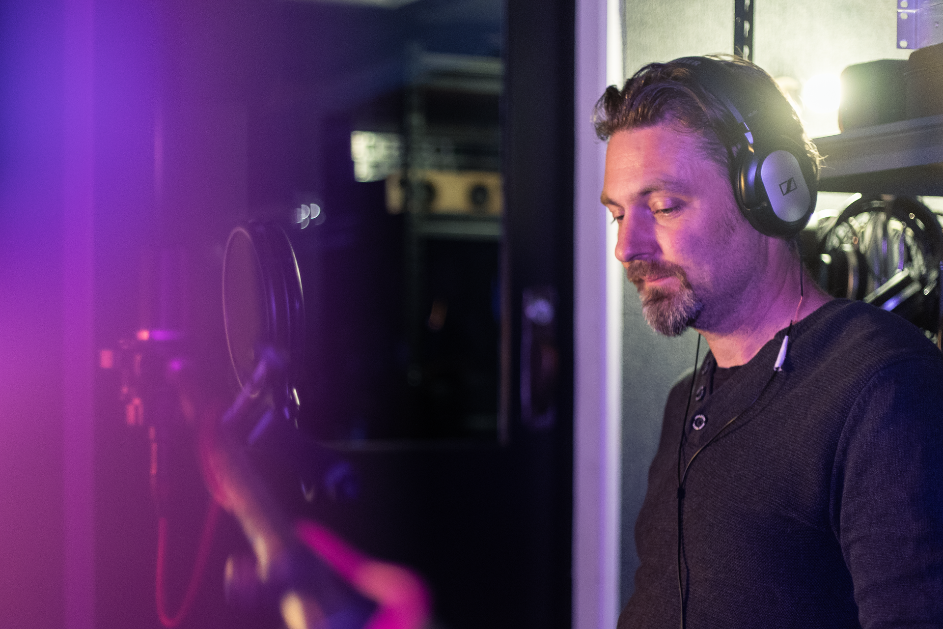 A man wearing headphones is standing in front of a microphone in a dark room.