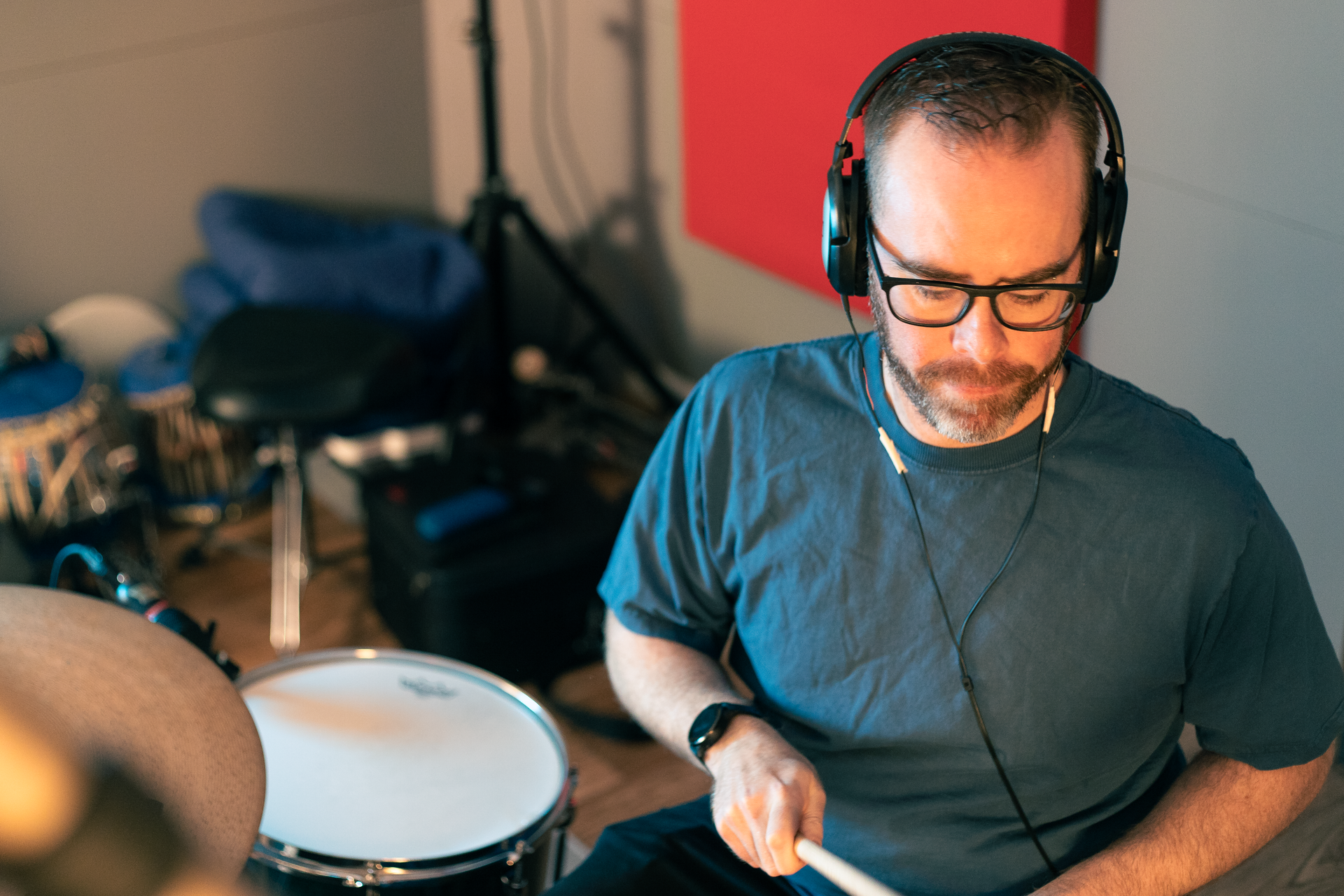 A man wearing headphones is playing drums in a room.
