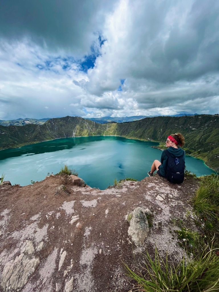 A woman is sitting on a rock overlooking a lake.
