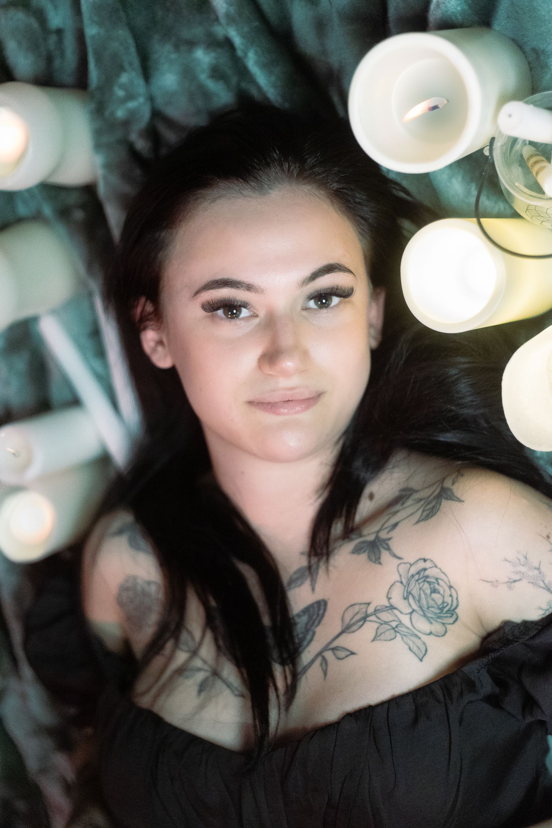 A woman with a tattoo on her chest is laying on a bed surrounded by candles.