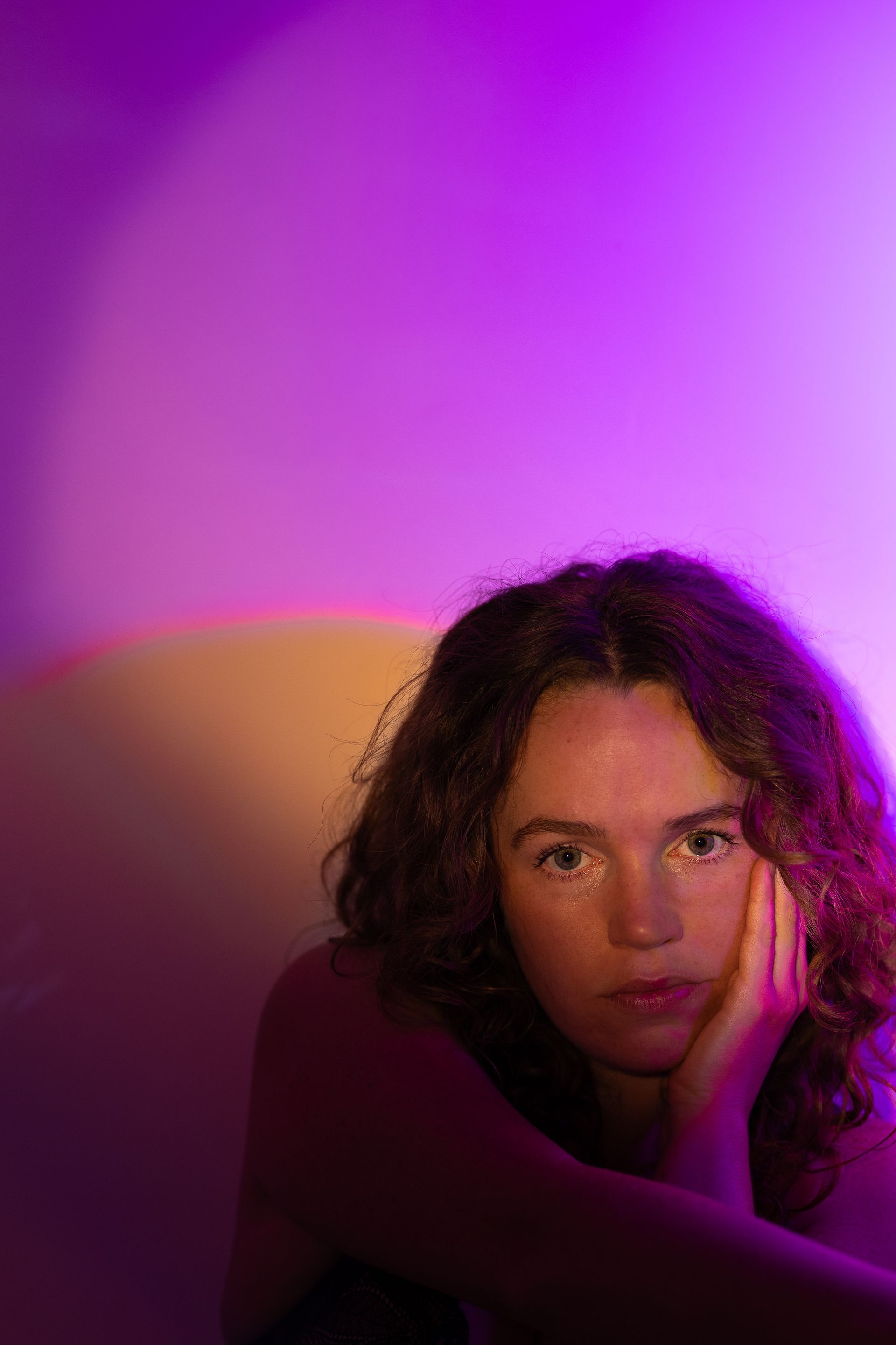 A woman with curly hair is sitting in front of a purple wall.