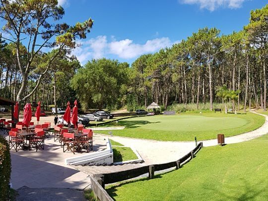 Un campo de golf con mesas, sillas y sombrillas en un día soleado.