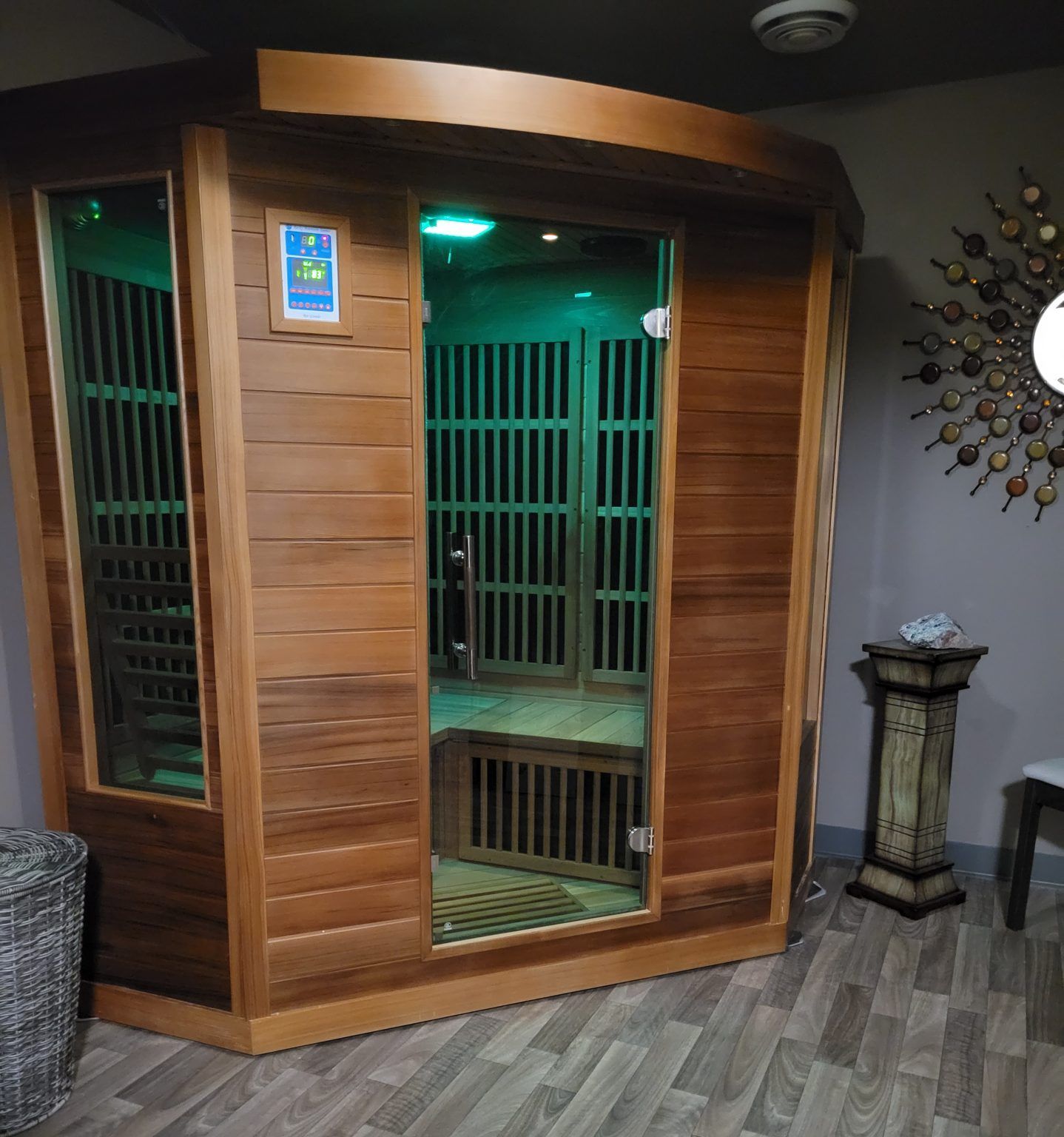 Wooden sauna with glass door, green interior lighting, and control panel.