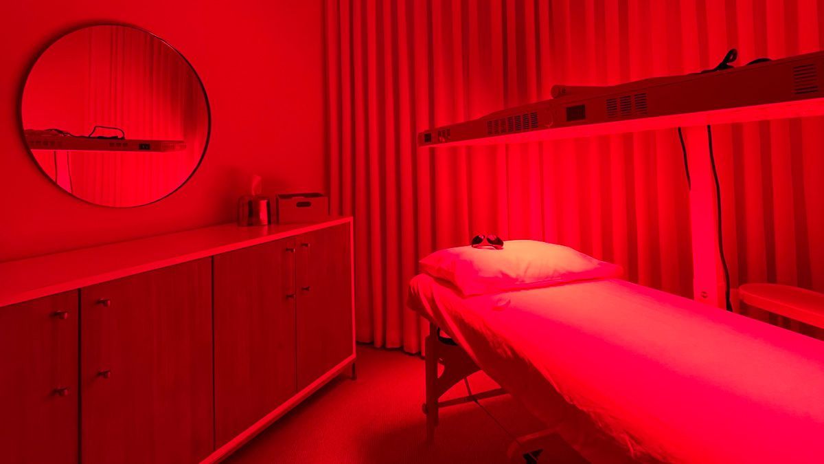 Red light therapy room with treatment table, mirror, and cabinetry.