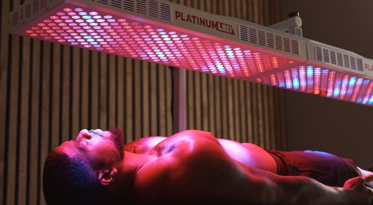 Person lying under pink and red neon lights beside a building with vertical slats.