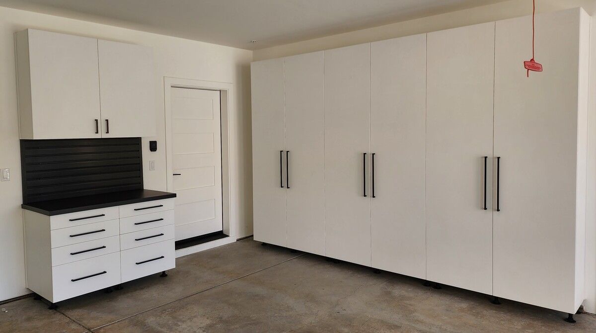 A garage with lots of white cabinets and drawers.