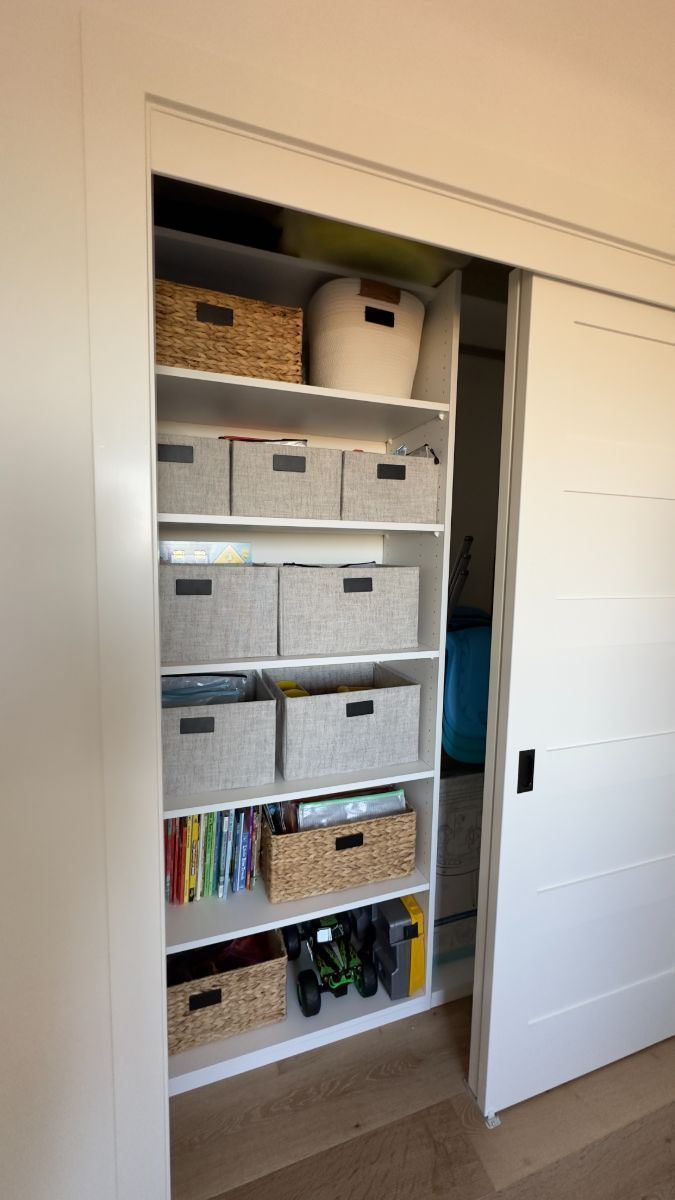 A closet filled with baskets and books and a sliding door.