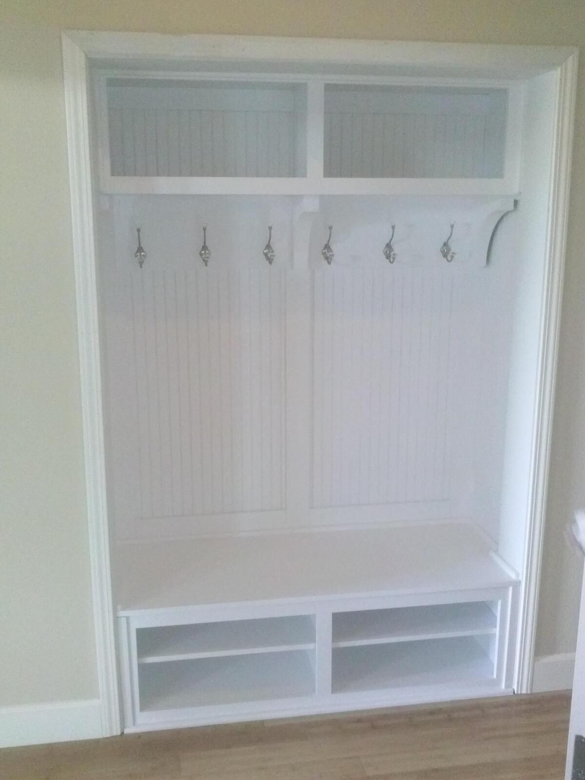 A white coat rack with hooks and shelves in a hallway.