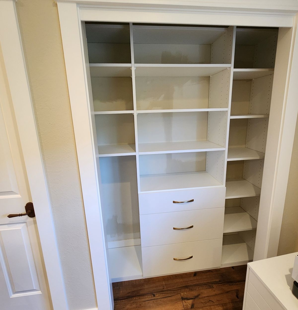 White built-in closet with shelves and drawers. Wooden floor, neutral walls.
