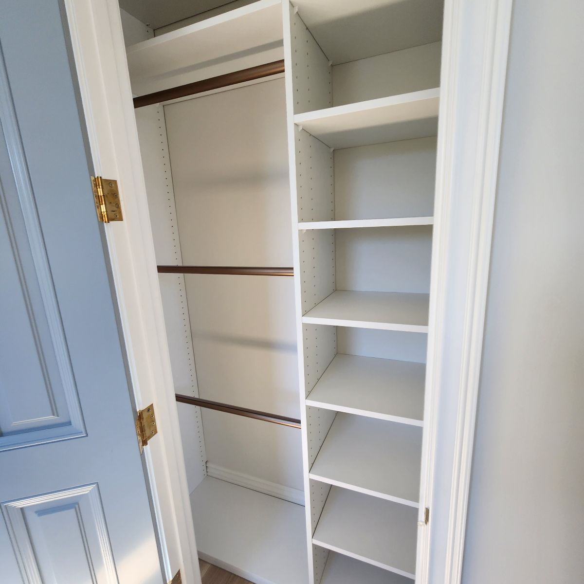 White Reach In closet interior with shelves and rods, door ajar, blue door frame, neutral wall.