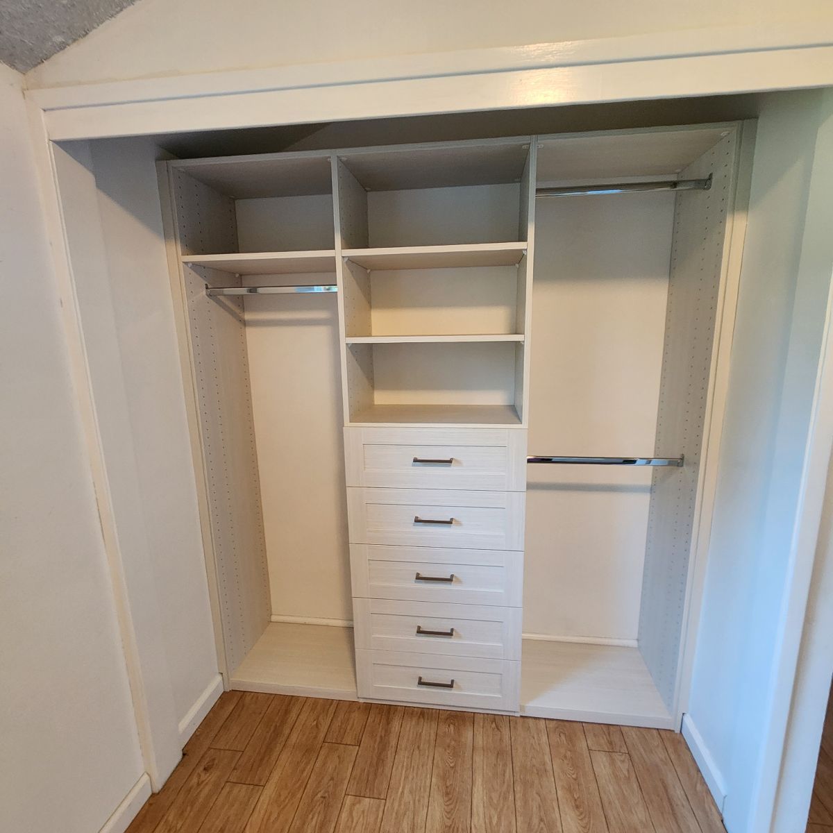White closet organizer with shelves, drawers, and hanging rods. Interior wood flooring.