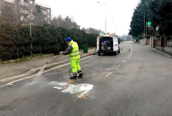 Un uomo con un gilet giallo sta spruzzando acqua su una strada.