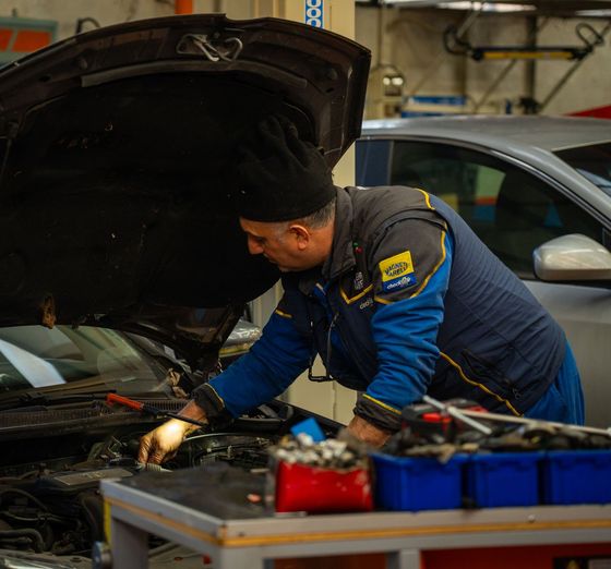 Un uomo sta lavorando su un'auto in un garage con il cofano aperto.