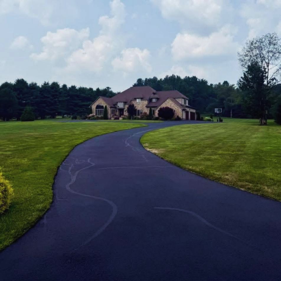 A sprawling residential home with a stone exterior sits at the end of a long, paved driveway surrounded by green lawns.
