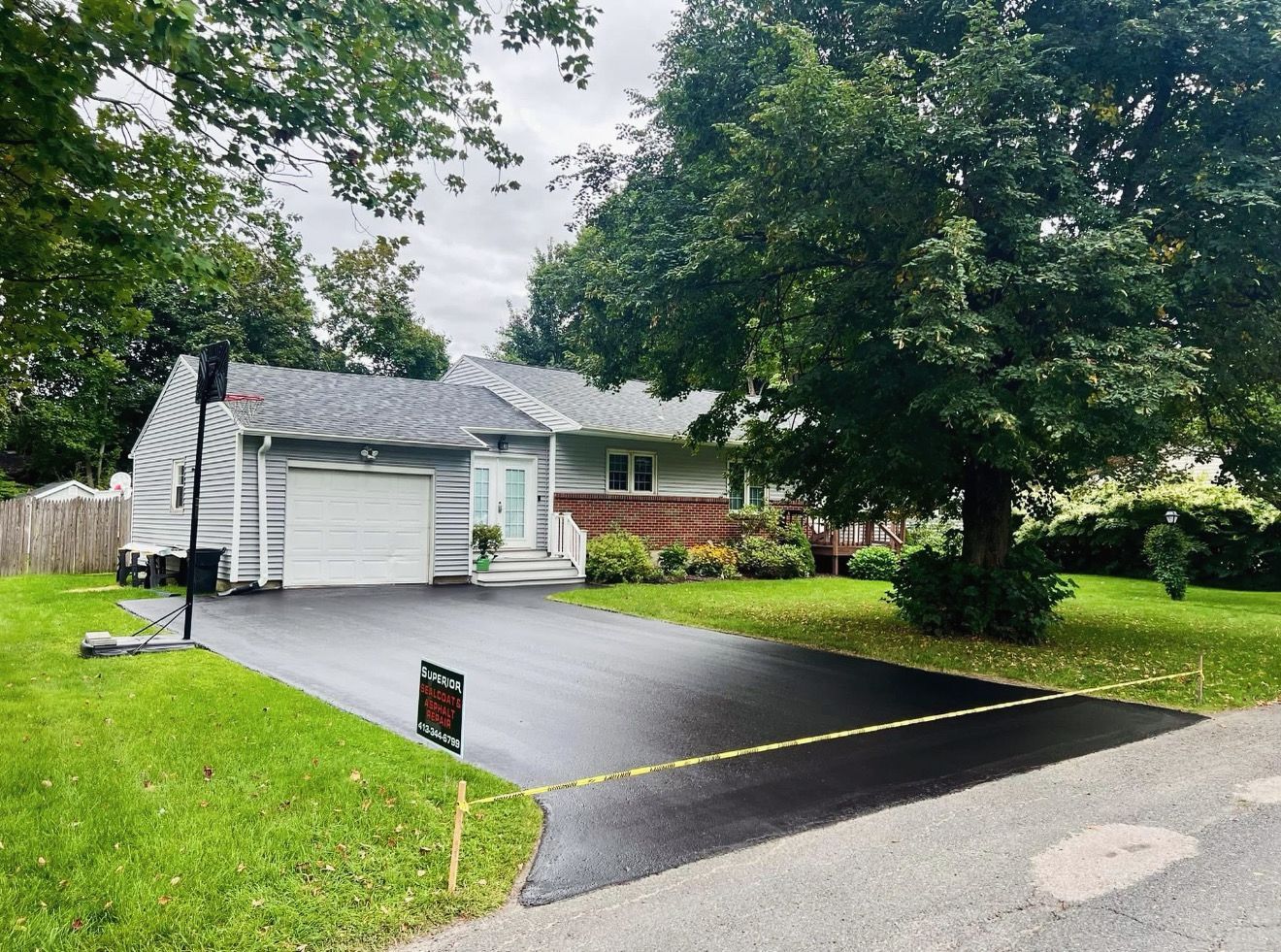 A suburban house with a light gray exterior, a white garage, and a newly paved dark asphalt driveway.