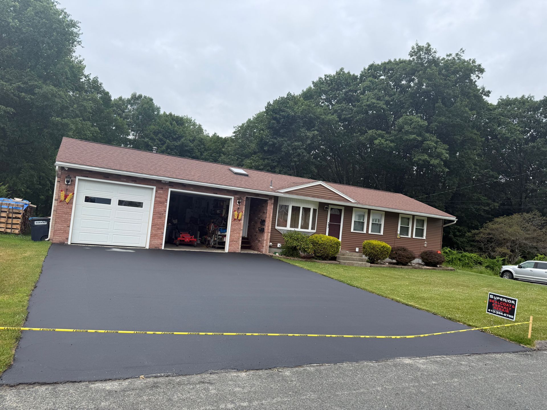 A newly paved asphalt driveway in front of a brick ranch-style house on a cloudy day.