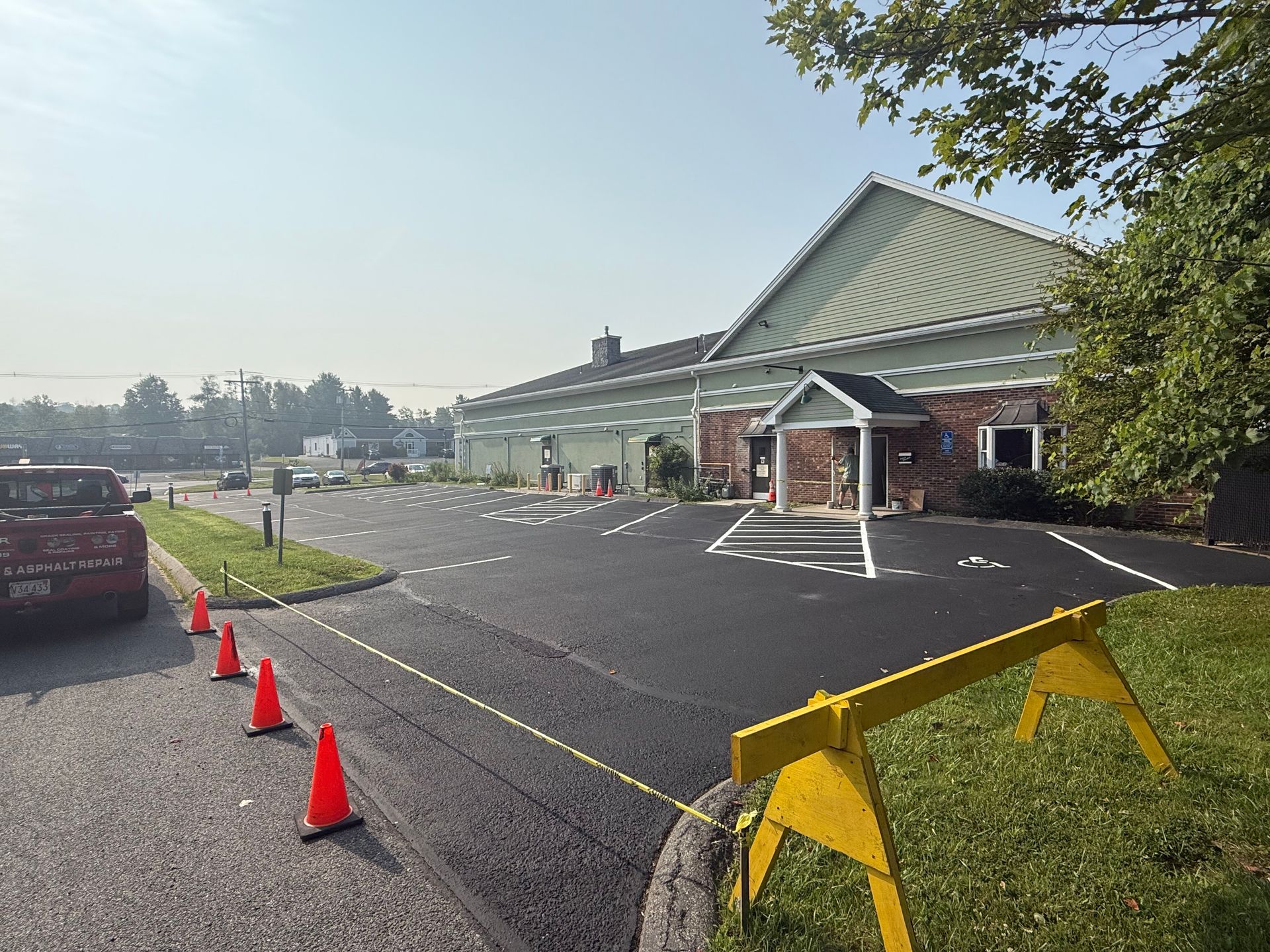 Freshly paved parking lot with new white striping, featuring orange safety cones and a yellow construction barrier.