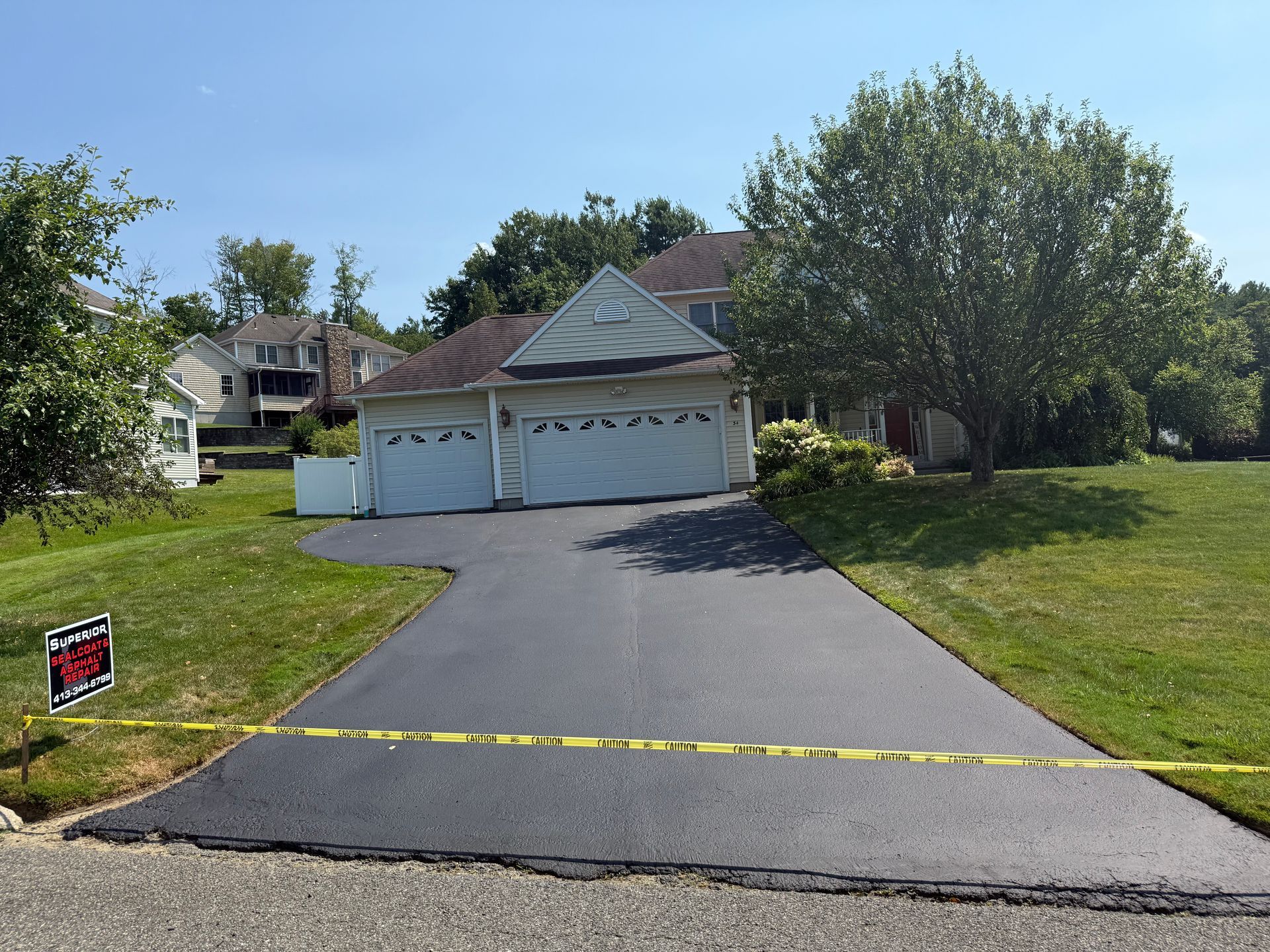 A freshly paved asphalt driveway leading to a two-car garage at a suburban home, marked off by yellow caution tape.